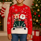 Child wearing a red Christmas sweater with reindeer and sleigh design, standing in front of a decorated Christmas tree and fireplace.