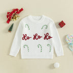 White Christmas Jumper with 'Ho Ho Ho' text and candy cane designs on a beige background with Christmas decorations.