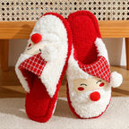 Red and white Santa Claus slippers with a smiling face design on a wooden surface.